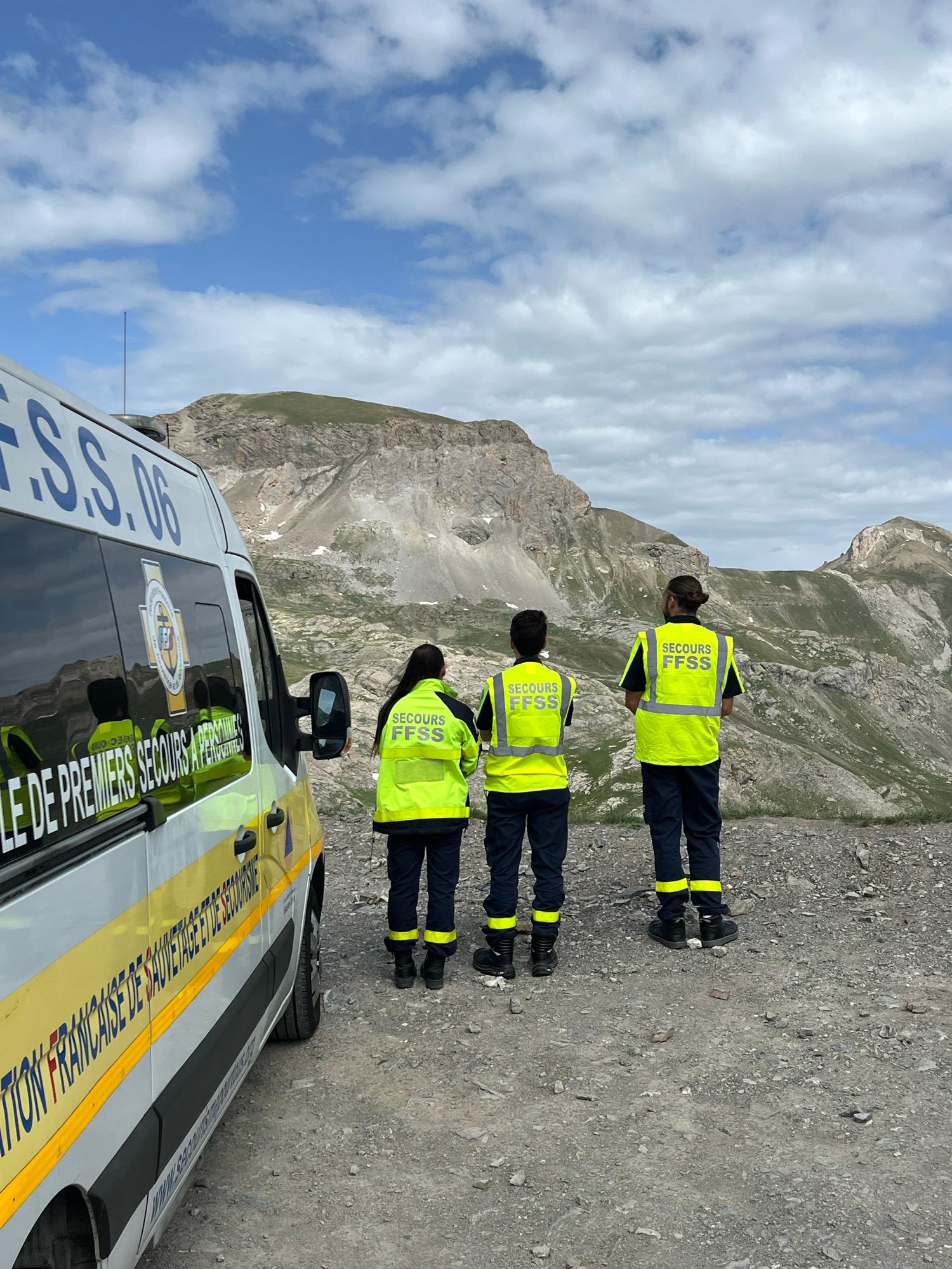 Trois secouristes de dos face à un col de montagne, à côté du véhicule de premiers secours à personnes de la FFSS 06.