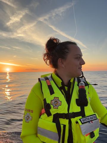 Annabell en gilet de sauveteur aquatique, face à la mer, au coucher du soleil.