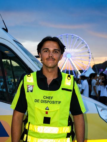 Thibaut en gilet « chef de dispositif », devant le véhicule de premiers secours, la grande roue de Nice éclairée en arrière-plan.